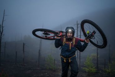 Mountainbiker mit Stirnlampe trägt sein Bike auf den Schulter.