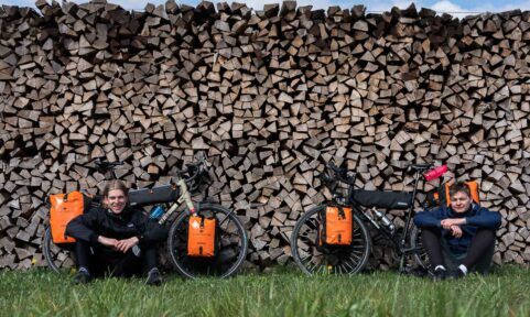 Gruppenbild von Linus und Justus mit ihrem Fahrrad vor einer Holzscheit-Wand